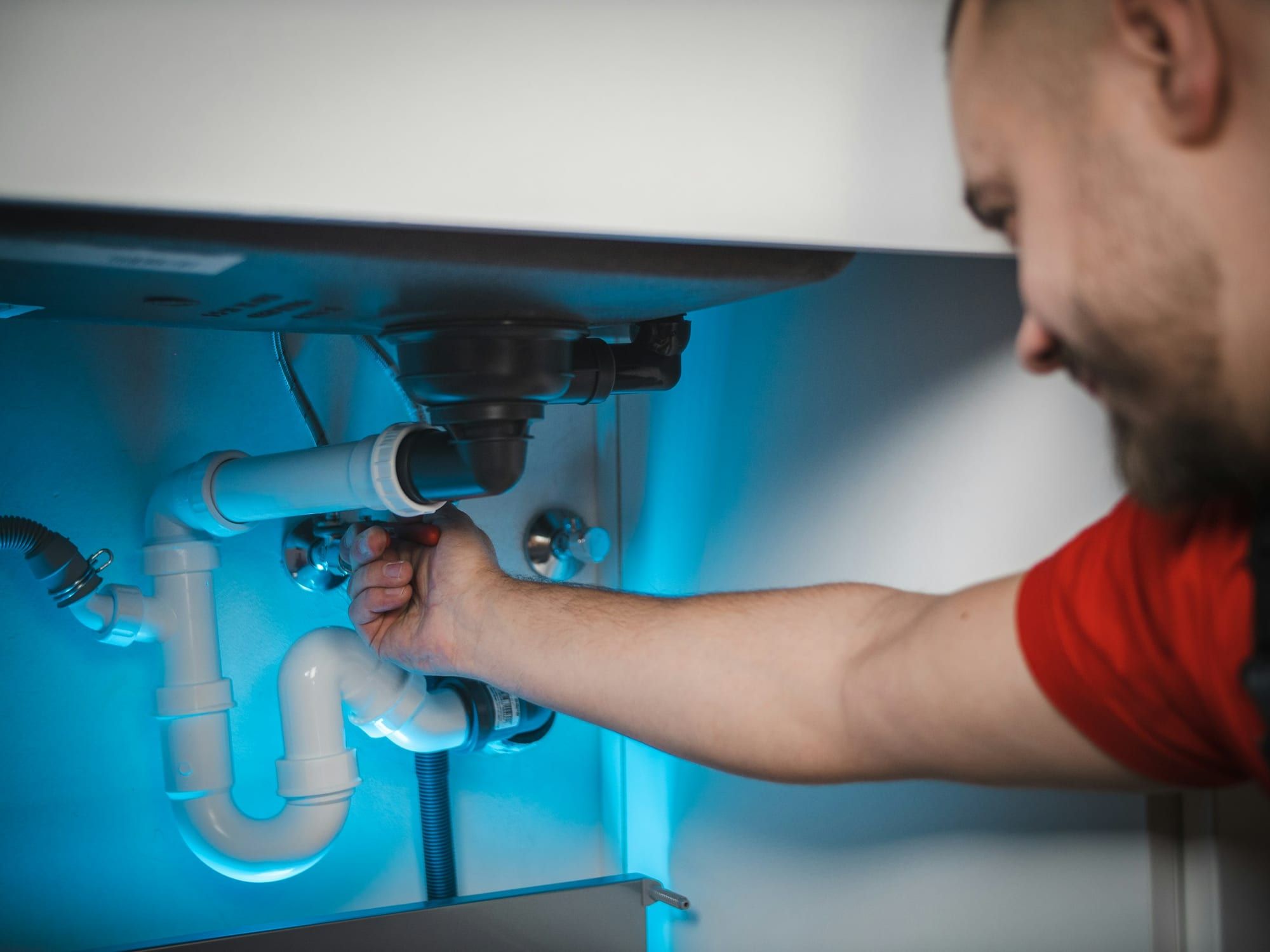 Plombier réparant le siphon d’un évier sous un meuble de cuisine